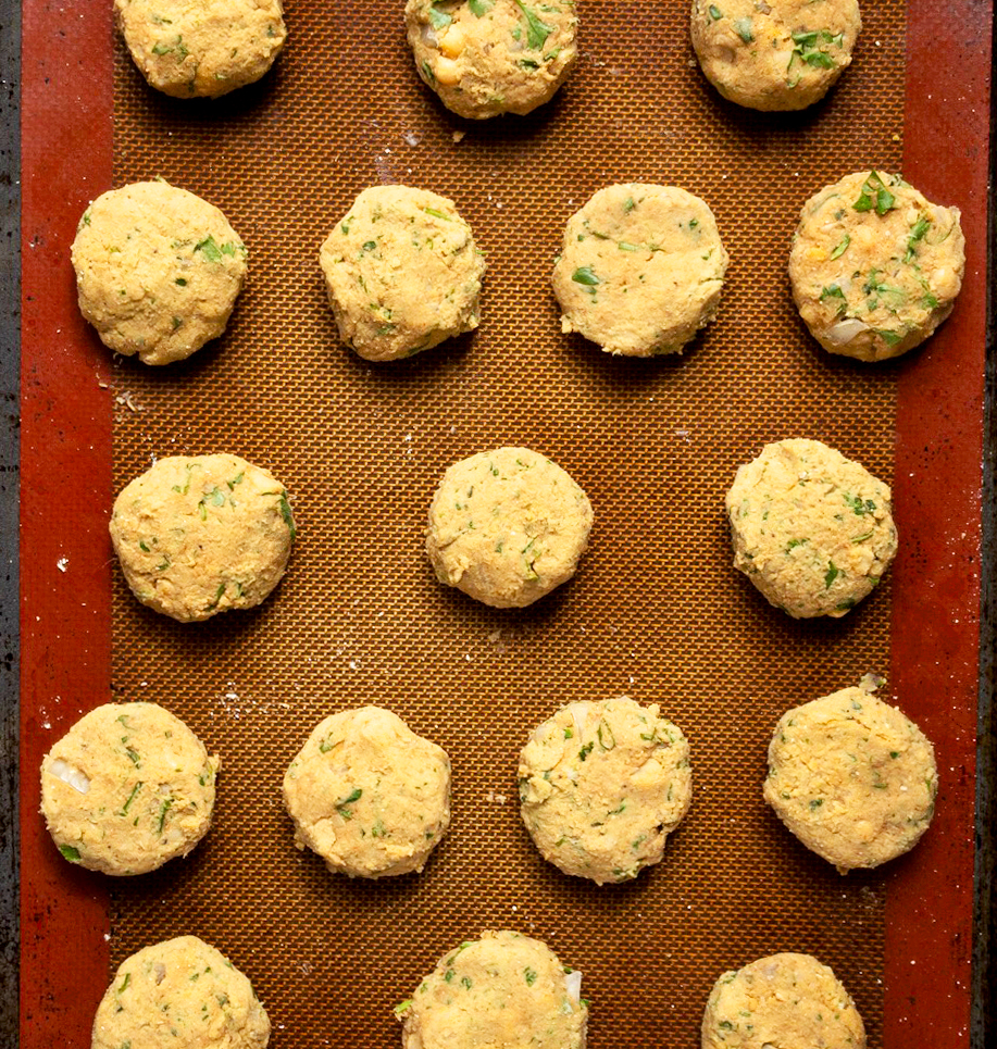 Uncooked balls of falafel dough on a silicone mat lined baking tray