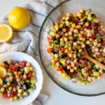 A large servings bowl of chickpea salad, with a smaller bowl of salad, and two lemons.