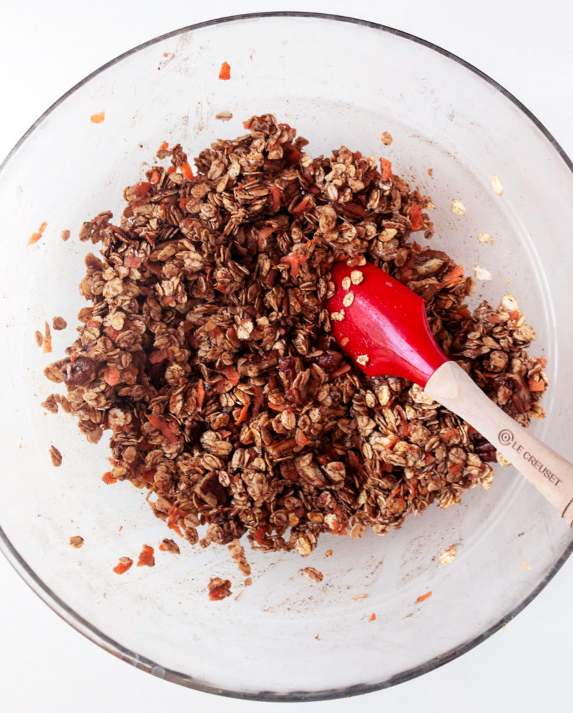 Glass bowl of uncooked carrot cake granola mixture with a red spatula