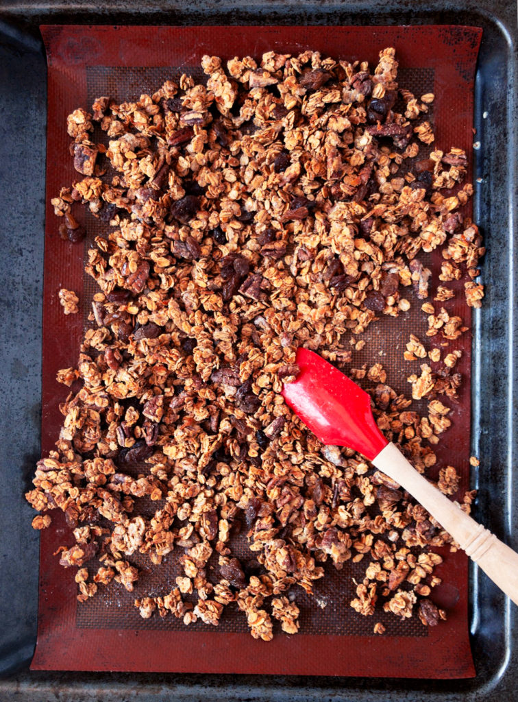 Silicone mat lined baking tray with baked Carrot Cake Granola cluster with a red spatula