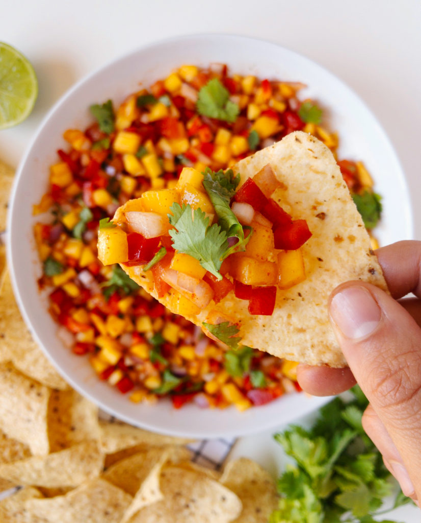 Hand holding a tortilla chip with the Mango Chili Salsa on it.