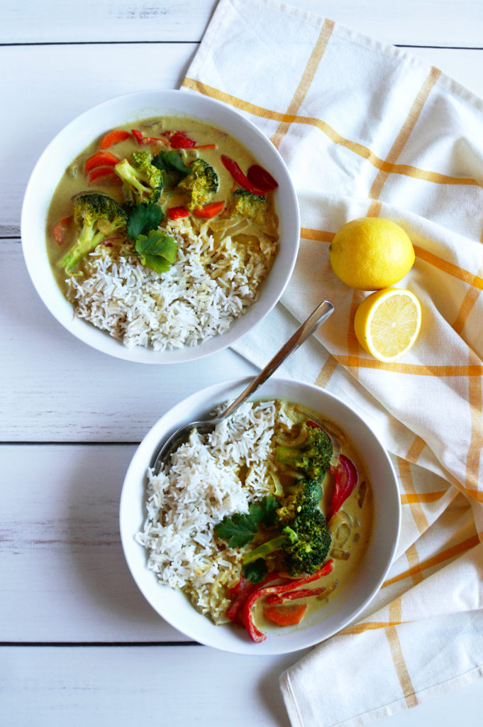 Two bowls of coconut curry on a white wooden table, with a white and orange striped tea towel and lemons.
