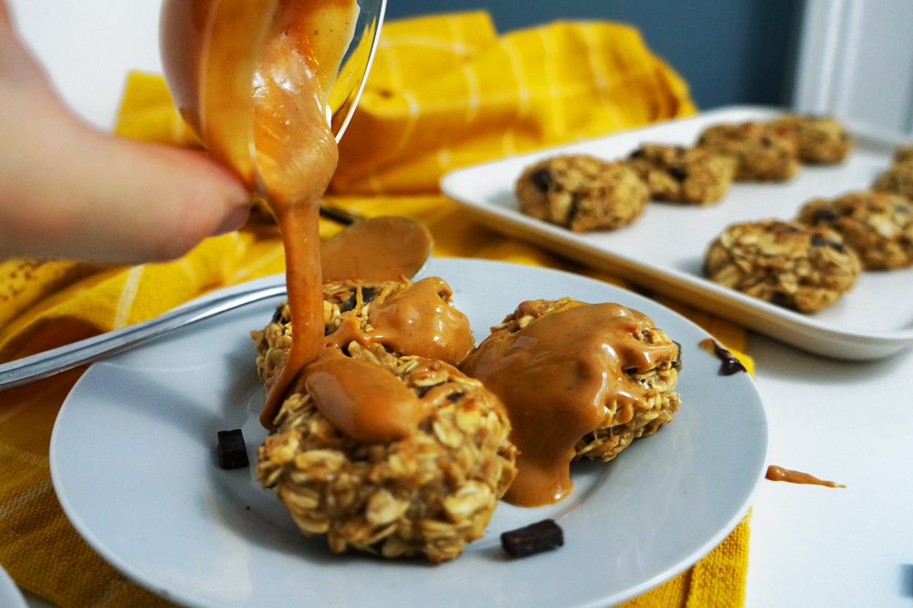 Vegan banana peanut butter chocolate oat breakfast cookies on a small white plate drizzled with smooth peanut butter.