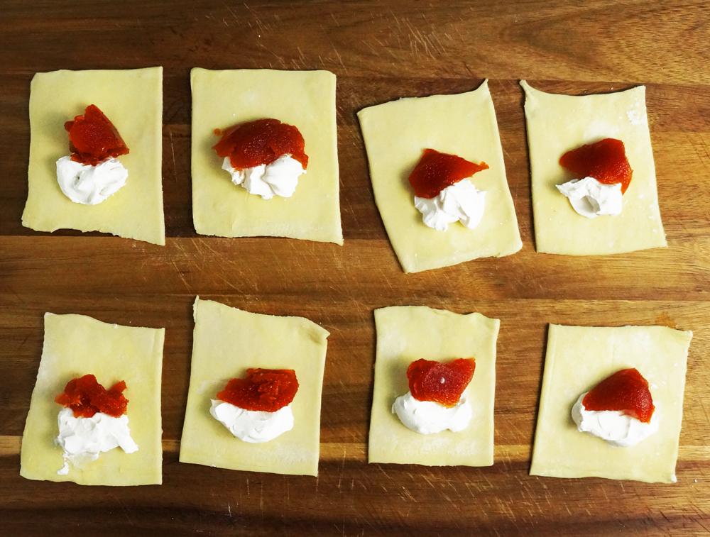 Uncooked puff pastry with guava paste and vegan cream cheese laid out on a wooden cutting board.