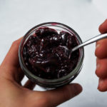 Vegan cherry chia jam being spooned out of a small glass jar.
