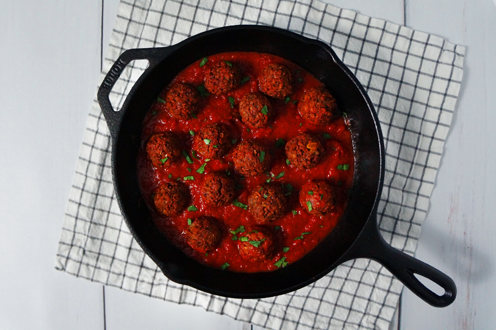 Vegan high-protein textured vegetable protein (TVP) meatballs in a cast iron skillet full of tomato sauce and topped with chopped parsley.