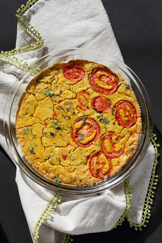 A great vegan pantry recipe – A large vegan chickpea frittata topped with sliced tomatoes in a glass container. 