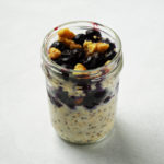 Jar of blueberry muffin oats, topped with blueberries and chopped walnuts.