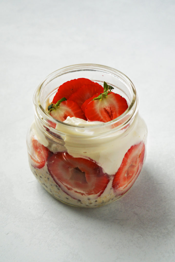 Jar of strawberries and cream oats, topped with sliced strawberries and vegan yogurt.