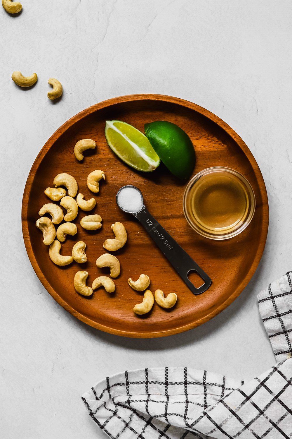 Ingredients to make vegan sour cream: cashews, salt, lime, and apple cider vinegar on a wooden plate. 