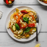 Creamy vegan pasta and sauteed summer veggies topped with fresh basil on a white plate.