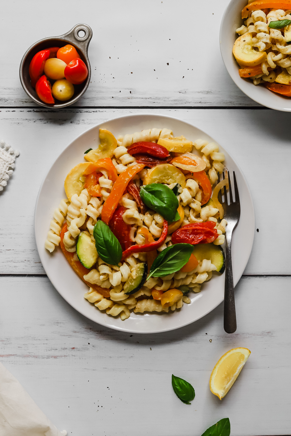 Creamy vegan pasta and sauteed summer veggies topped with fresh basil on a white plate.