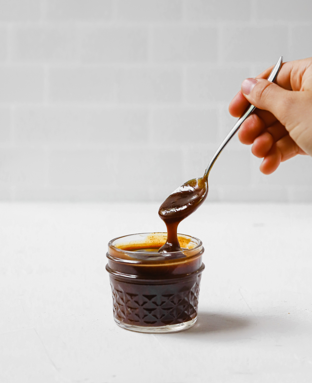 Sticky teriyaki sauce dripping off a spoon into a jar. 