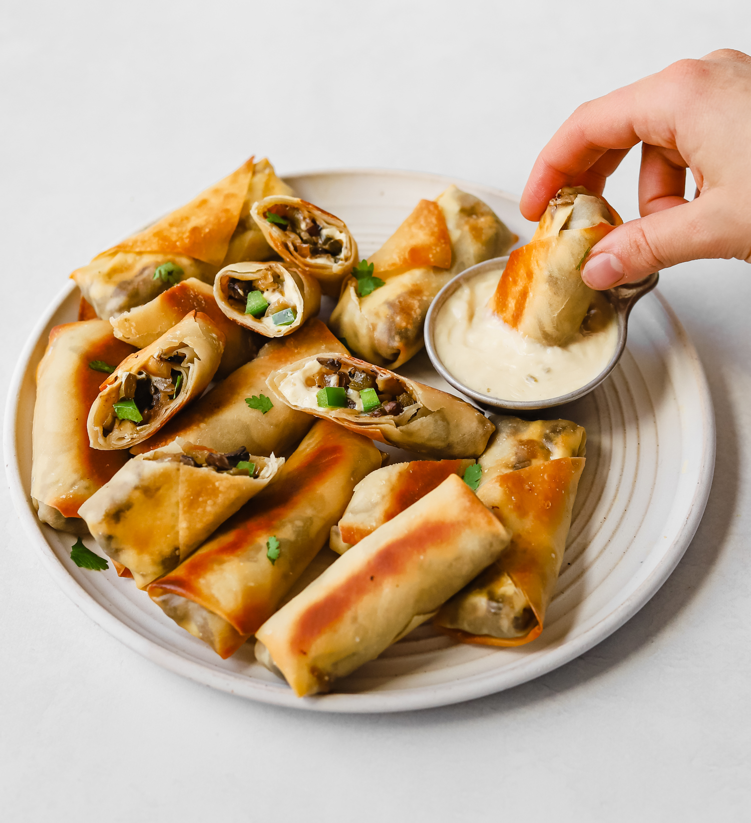 Dipping a mushroom philly cheesesteak egg roll into vegan cheese dipping sauce