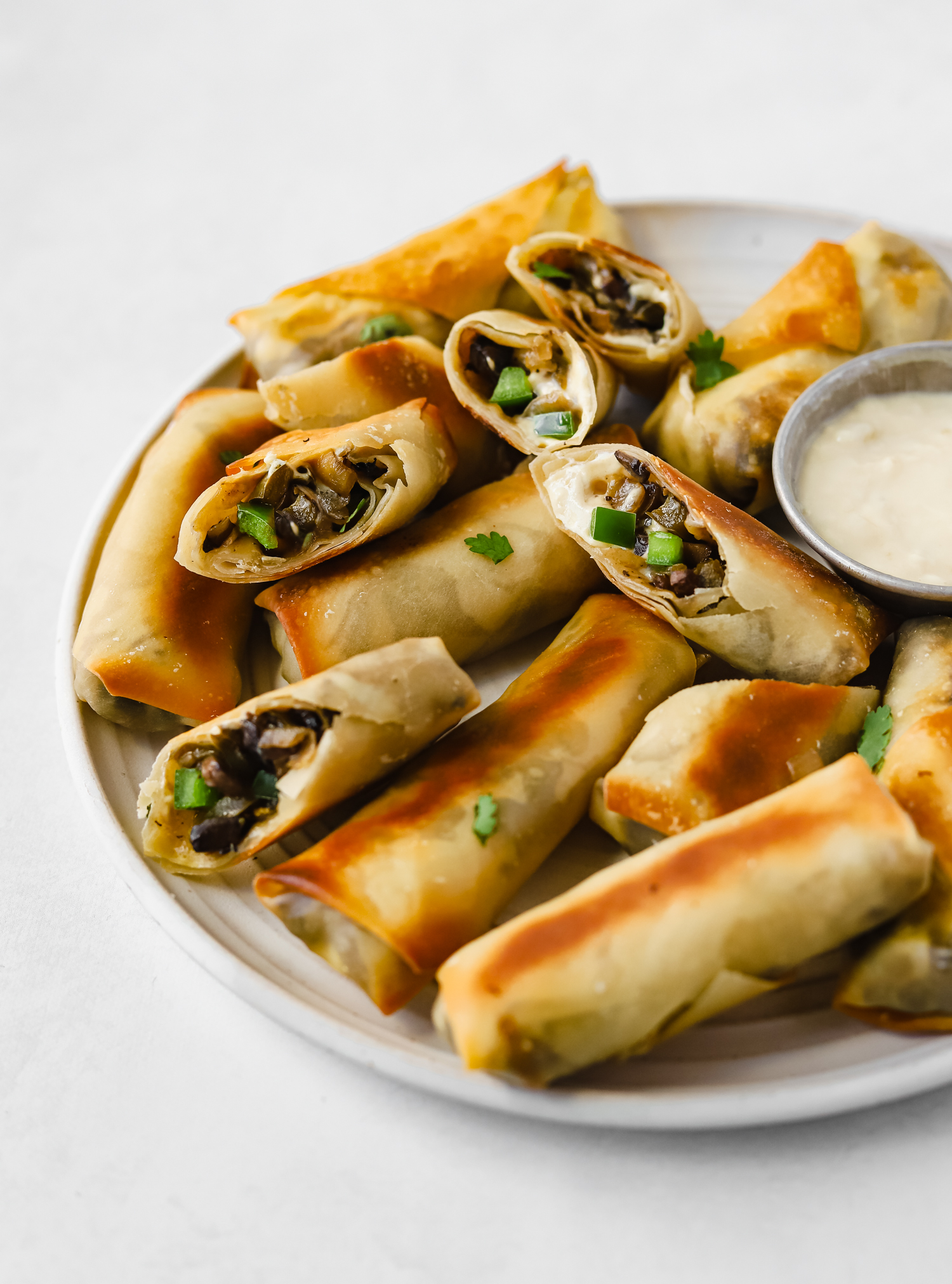 A plate of vegan philly cheesesteak egg rolls with a cheese dipping sauce on a white plate