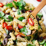 Light and healthy greek pasta salad with olives, cucumber, tomatoes, artichokes, onions, and vegan feta