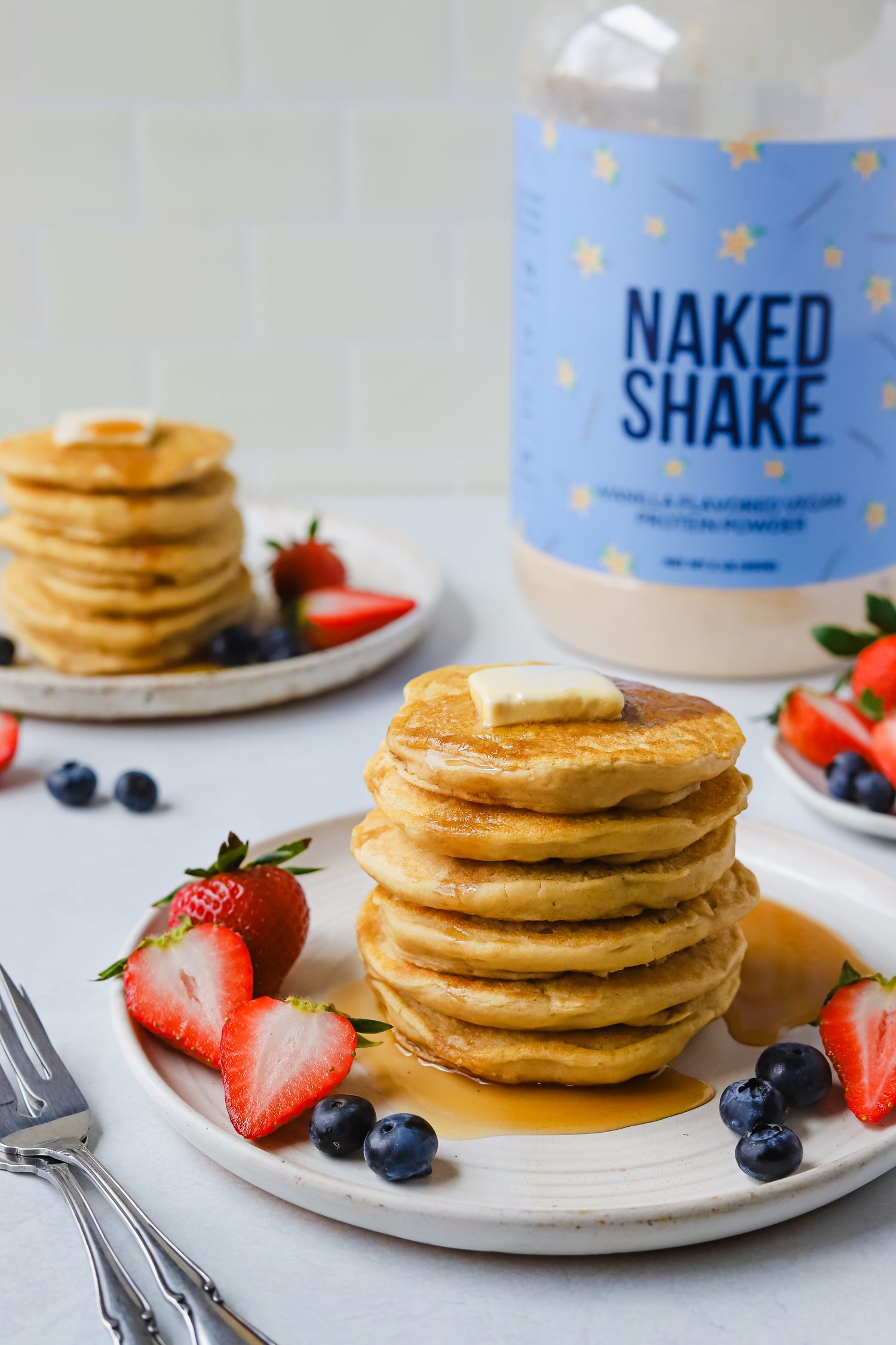vegan pancakes on a white plate with strawberries, blueberries, and Naked Shake vanilla vegan protein powder